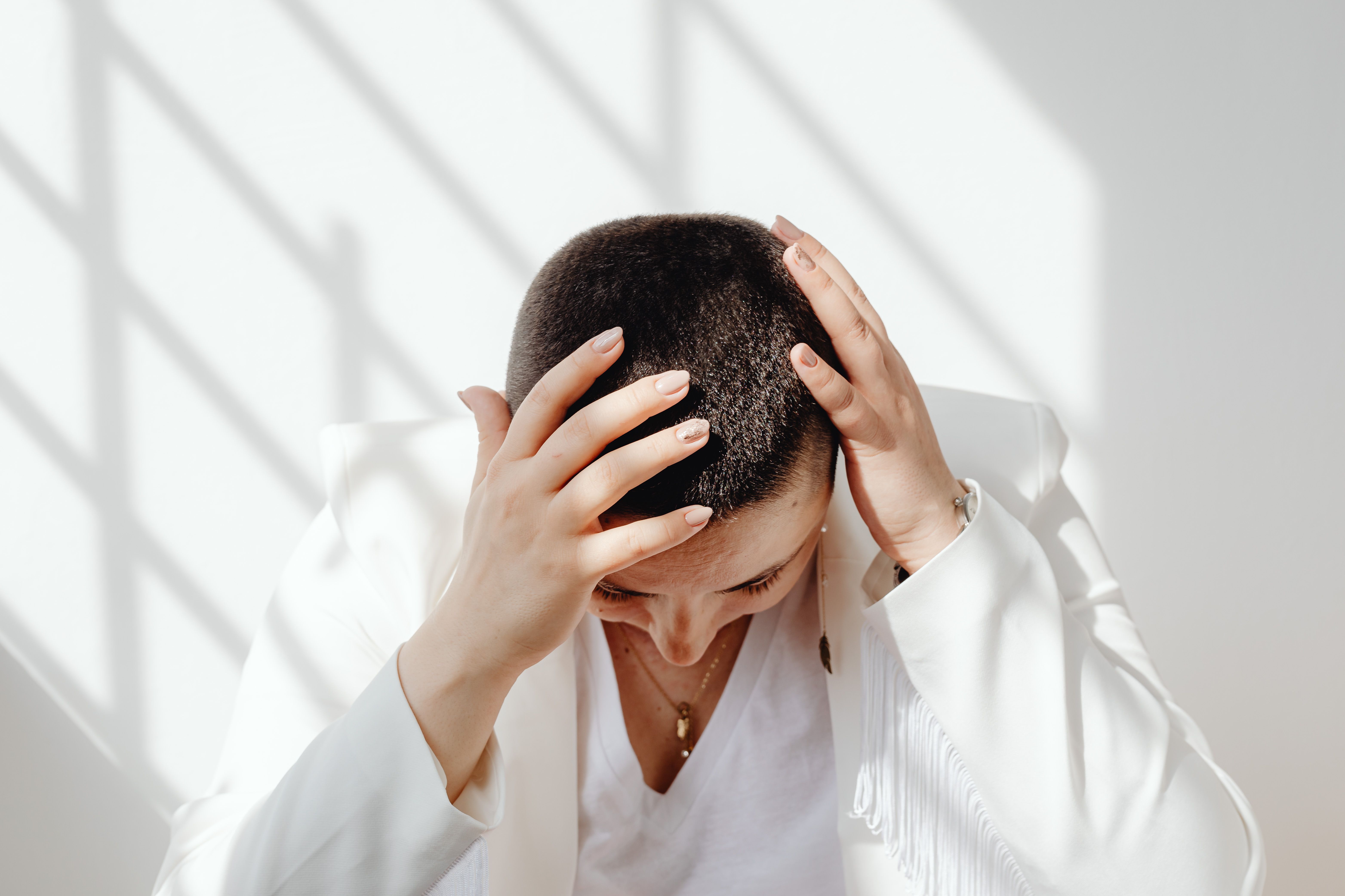 Stressed woman sitting indoors with her hands on her head, representing stress-related hair shedding.