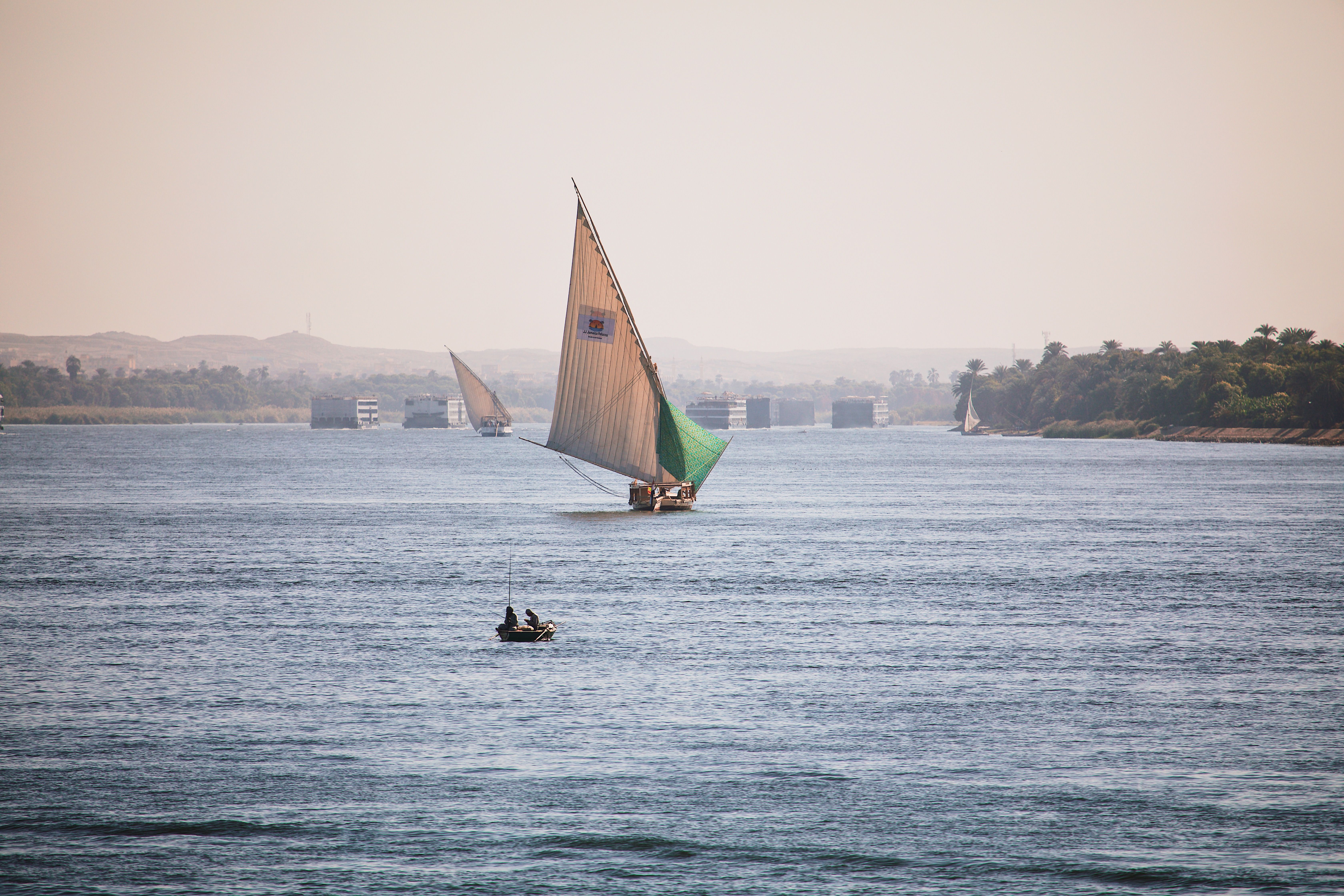 A traditional felucca sails on the Nile in Luxor beneath a clear sky.